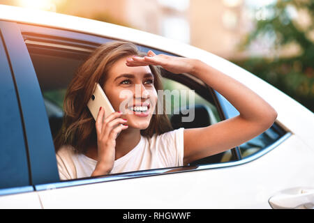 Beautiful woman with phone smiling while sitting on the back seat in the car. Stock Photo