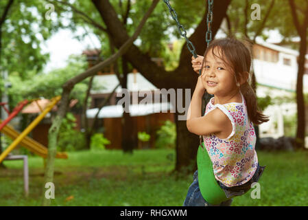 Asian girl on a swing looking at the camera. Filipina girl. 6 to 7 years old. Stock Photo