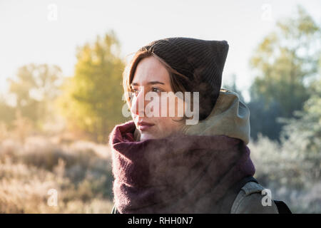 Backlit portrait of beautiful breath misting woman. Female person walking outdoors on chilly sunny morning in autumn Stock Photo