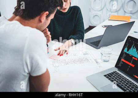 Two architect design concept blueprint. Young man and woman designer sketching a construction project at laptop and drawing plan while working at offi Stock Photo