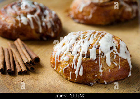 3 iced cinnamon rolls on wooden surface with cinnamon sticks. Stock Photo