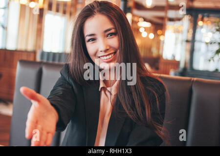 Beautiful charming brunette happy asian girl young woman giving handshake, hand of help, greeting at cafe Stock Photo