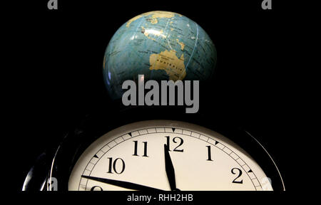 Globe emerging above a clock Stock Photo