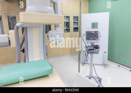 Vital signs monitor and large C-arm angiograph, operating room with X-ray medical scan in hospital. Stock Photo