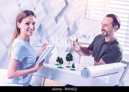 Beautiful woman making notes while sitting with her colleague and smiling Stock Photo