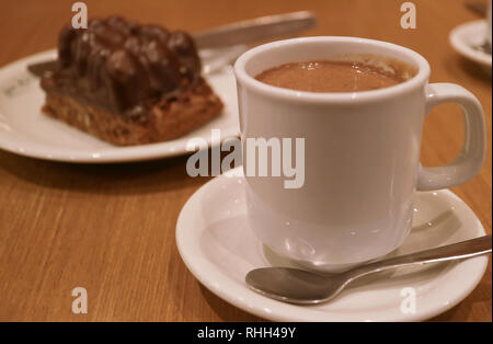 A cup of hot chocolate with a plate of blurry chocolate cake served on wooden table Stock Photo
