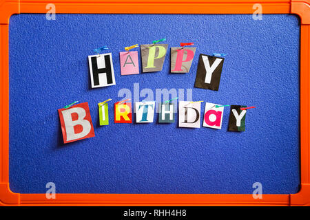 Happy birthday letters cut from magazine pinned on blue background Stock Photo