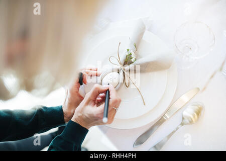 Preparing simple festive Easter table setting with napkin Easter Bunny for one person. Old woman drawing his face. Stock Photo