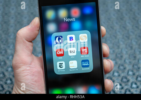 Male hand holding Black Apple iPhone with icons of News media: Guardian, Bloomberg, BBC News, CNN, NY Times, Euronews and other application on screen. Stock Photo