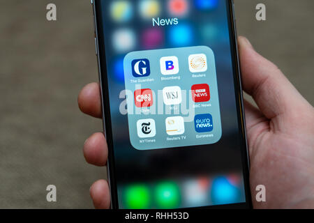 Male hand holding Black Apple iPhone with icons of News media: Guardian, Bloomberg, BBC News, CNN, NY Times, Euronews and other application on screen. Stock Photo
