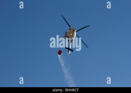 Helicopter extinguishing forest fires, heading to a fire spilling water from a basket that transports. Stock Photo