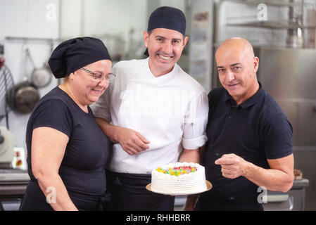 Smiling pastry Chefs team showing a cake. Stock Photo
