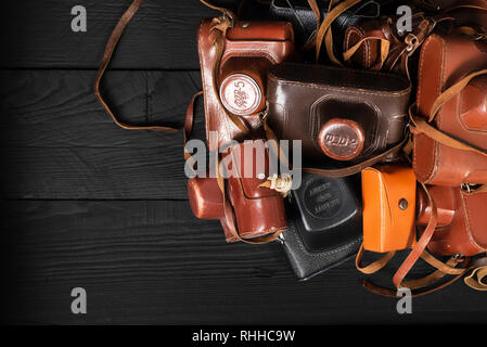 Drohobych, Ukraine - 02 February, 2019: Heap of 35mm retro cameras in leather covers on black, top view Stock Photo