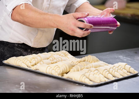 Pastry chef sealing with plastic film a tray of croissants dough . Stock Photo