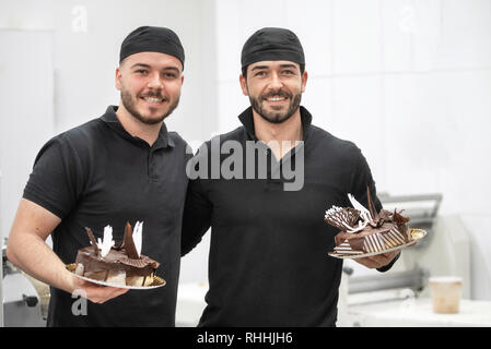 Portrait of two pastry chefs smiling with cakes in his hands, working together . Stock Photo
