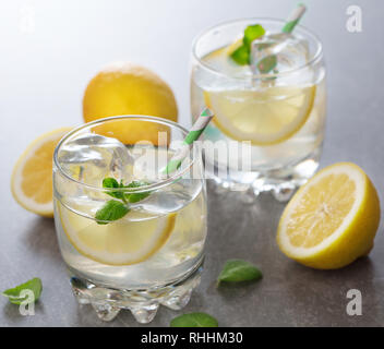 two glasses of lemonade with ice, mint and cut lemons on gray background Stock Photo