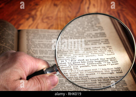 Hand holding magnifying glass over an old Bible opened to the famous verse of John 3:16. This translation is King James, which is public domain. Stock Photo