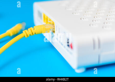 home wireless router with ethernet cable plugged in on blue background, close up Stock Photo