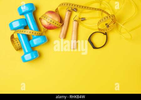 Fitness concept with blue dumbbells, jump rope and fitness tracker on yellow background, top view flat lay Stock Photo