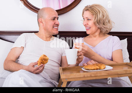 Positive smiling senior spouses having healthy breakfast in bed in the morning Stock Photo