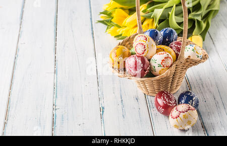 Easter eggs in basket and spring tulips on wooden table. Stock Photo