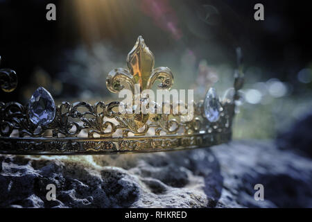 mysterious and magical photo of gold king crown over the stone in the England woods or field landscape with light flare. Medieval period concept Stock Photo