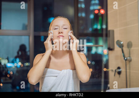 Beautiful woman removes makeup on the background of a window with a panoramic view of the night city Stock Photo