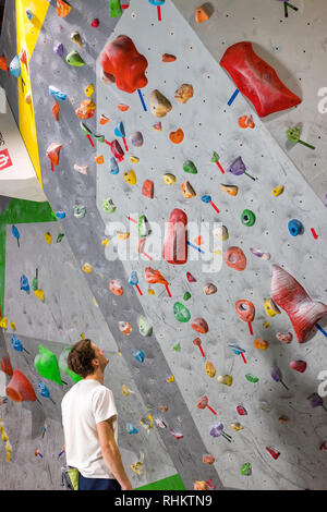 Rock climber stands and looks at the climbing wall with hooks in the boulder hall Stock Photo