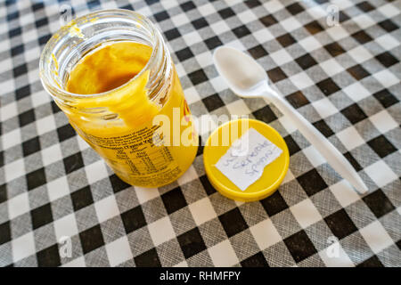 Colmans English Mustard jar with lid off and plastic spoon on a black and white plastic gingham table cloth on a cafe table in england Stock Photo