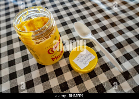 Colmans English Mustard jar with lid off and plastic spoon on a black and white plastic gingham table cloth on a cafe table in england Stock Photo