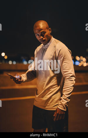 Sportsman standing oudtoors with mobile phone. Fintess man taking break after workout outdoors at night. Stock Photo