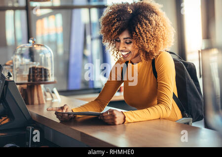 Tourist woman standing at the billing counter of a cafe holding the menu card. Smiling tourist wearing backpack talking to the cafe owner looking at t Stock Photo