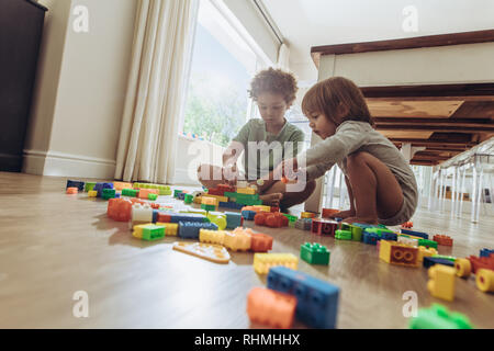 Two kids sitting on floor and playing with building blocks. Siblings playing with toys at home. Stock Photo