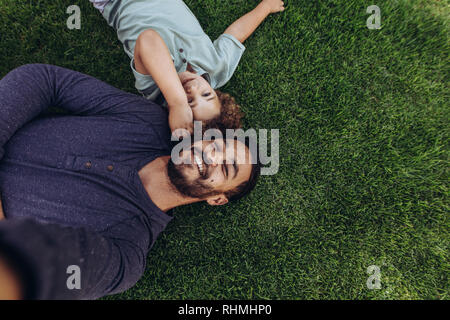 Man lying on grass in a park with his son. Top view of father and son lying on ground at a park with heads together.