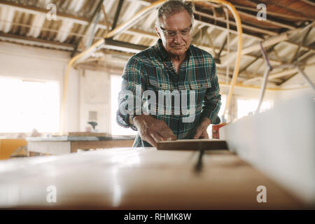 Senior male carpenter working on table saw machine. Man cutting wood planks on table saw machine in carpentry workshop. Stock Photo