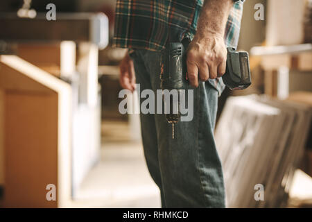 Carpenter holding a hand drill machine at workshop. Cropped shot of man with drilling machine in hand at carpentry workshop. Stock Photo