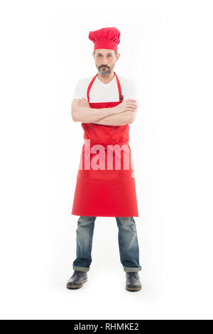 Known for his cooking. Bearded mature man in chef hat and apron. Senior cook with beard and moustache wearing bib apron. Mature chief cook in red cooking apron. Home cooking. Stock Photo