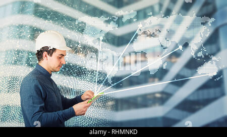 Side view man engineer wearing protective helmet using a tablet computer gadget choosing destinations on the world map. Modern technology artificial i Stock Photo