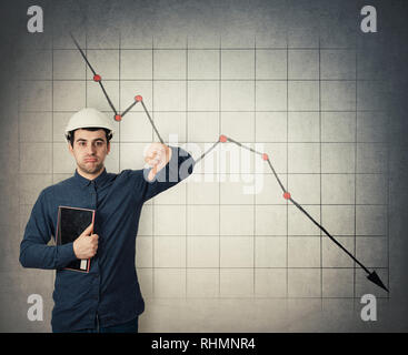 Unhappy and tired young man engineer wearing protective helmet holding tablet computer showing thumb down negative gesture looking bored and a decreas Stock Photo