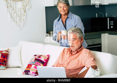 Senior adult caucasian couple at home using laptop modern internet computer and having some good time together in married lifestyle - kitchen in backg Stock Photo