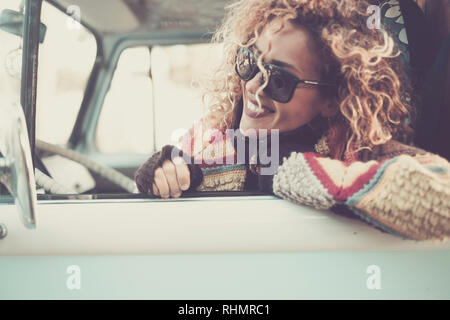 Cheerful happy beautiful caucasian young woman looking and smiling out of the window from old vintage van bus with sunglasses - travel driving concept Stock Photo