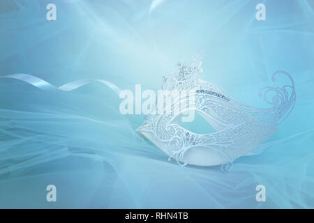 Photo of elegant and delicate white lace venetian mask over blue chiffon background Stock Photo
