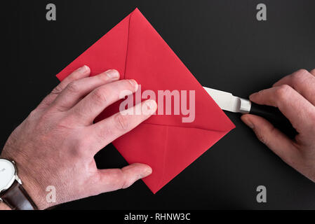 hands of man opening red envelope with paper knife Stock Photo