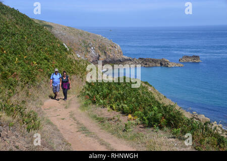 A Couple of Hikers Walking in Sunshine on the Coastal Path Towards Rosiere Steps on Herm Island,  Channel Islands.UK. Stock Photo