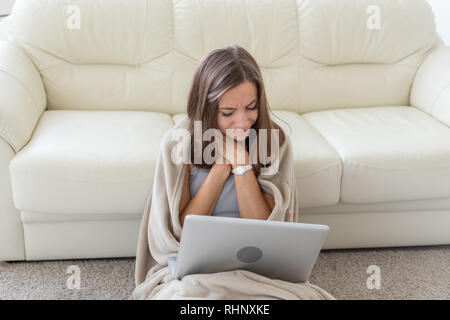 Woman having a sore throat sitting on the floor with laptop Stock Photo