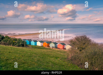 Impressive winter clouds in a cool blue sky over the beach huts and natural spit of land that stretches out to sea on the beach in Tankerton, Whitstab Stock Photo