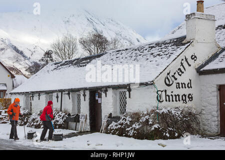 Walkers head for Crafts and Things shop and café covered in snow on a cold winters day at Glencoe Village, Highlands, Scotland in winter