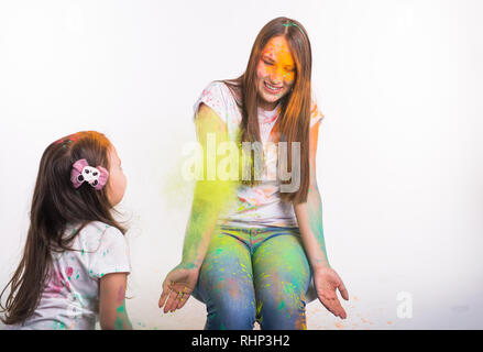 Festival of holi, people and holidays concept - Little girl playing with her mother covered with yellow dust over white background Stock Photo