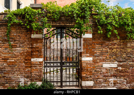 A wrought iron gate and brick wall in front of a medieval courtyard in the historic center of Venice, Italy Stock Photo