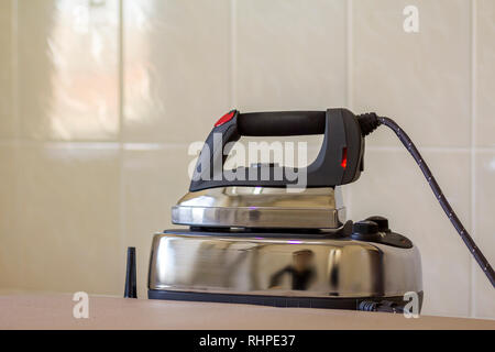 Close-up of new modern stainless steel iron with teflon sole and with steam generator isolated on iron plate on light copy space background. Stock Photo